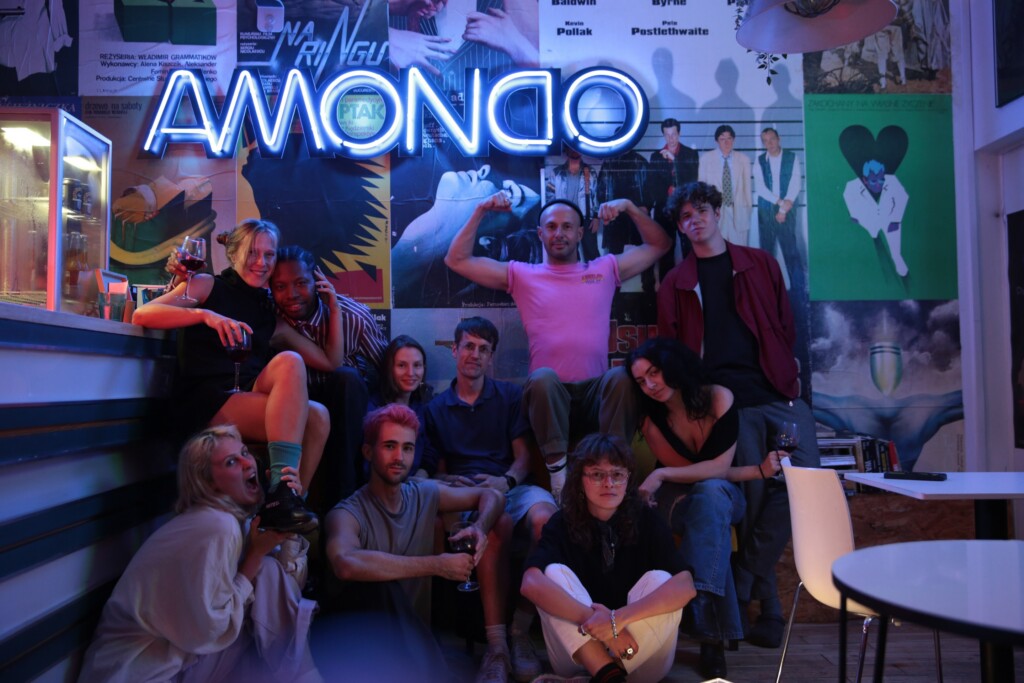 Group of friends posing for a photo in a neon-lit bar with colorful posters on the wall and several holding drinks.