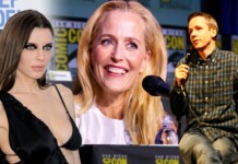 Panel at Comic-Con featuring three speakers: a woman in a black dress on the left, a smiling blonde woman center, and a man in a plaid shirt speaking into a microphone on the right, with Comic-Con banners in the background.