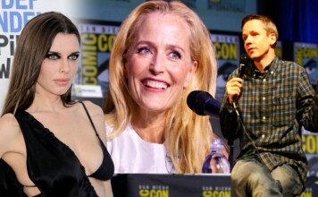 Panel at Comic-Con featuring three speakers: a woman in a black dress on the left, a smiling blonde woman center, and a man in a plaid shirt speaking into a microphone on the right, with Comic-Con banners in the background.