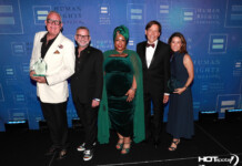 Five adults in formal attire posing together on a stage with a blue Human Rights Campaign backdrop; two men hold clear glass trophies.