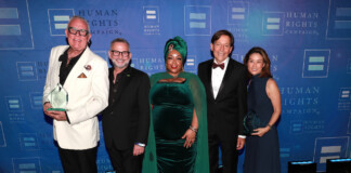 Five adults in formal attire posing together on a stage with a blue Human Rights Campaign backdrop; two men hold clear glass trophies.