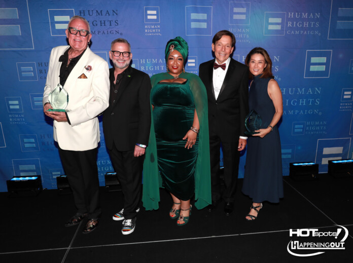 Five adults in formal attire posing together on a stage with a blue Human Rights Campaign backdrop; two men hold clear glass trophies.