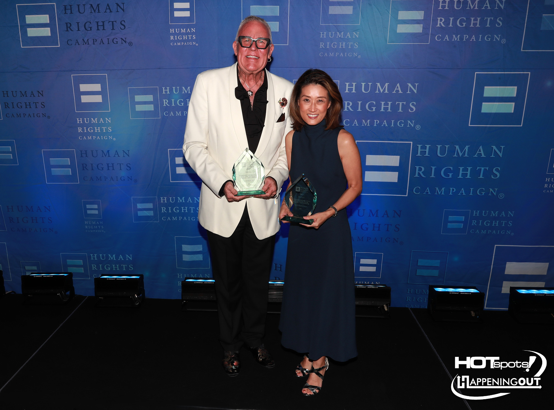 Two award recipients pose on a blue backdrop holding glass trophies at a Human Rights Campaign event.
