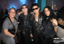 Four friends posing together in a nightclub, wearing dark rock-style outfits and sunglasses, with blue and purple lighting in the background.