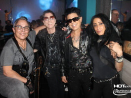 Four friends posing together in a nightclub, wearing dark rock-style outfits and sunglasses, with blue and purple lighting in the background.