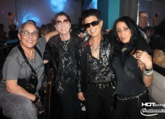Four friends posing together in a nightclub, wearing dark rock-style outfits and sunglasses, with blue and purple lighting in the background.