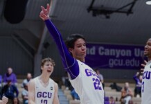 GCU basketball player in white jersey #22 raises his arm in triumph while teammates cheer on the court.
