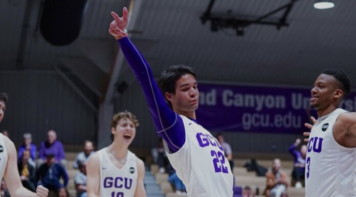 GCU basketball player in white jersey #22 raises his arm in triumph while teammates cheer on the court.