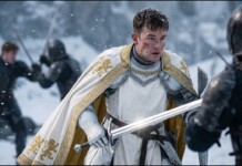 Knight in white armor with a gold-embroidered cape faces an opponent in a snowy battlefield, sword drawn.