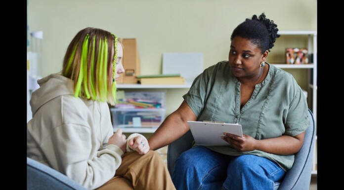 Supreme Court Declines Review of School’s Handling of Student Gender Identity Request Two people in a counseling session: a clinician with a clipboard speaks with a person wearing a beige hoodie and neon green hair.