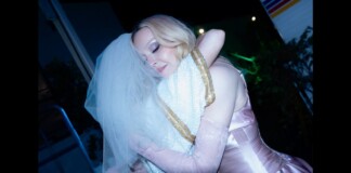 Two women hug at night; one wearing a veil and sequined dress, the other in a pink satin gown.