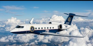 FBI business jet in flight above white clouds and a mountain range.