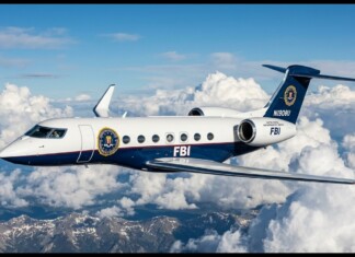 FBI business jet in flight above white clouds and a mountain range.