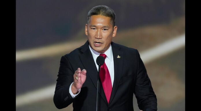 Hung Cao Has Been Named Acting Secretary Of The Navy. Witches And Drag Queens Worry Him A Lot Man in a black suit and red tie speaks into a microphone at a podium, gesturing with his left hand on a dark stage backdrop