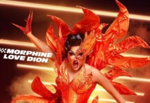 Drag performer in a fiery orange costume with dramatic makeup, posing against streaks of light.