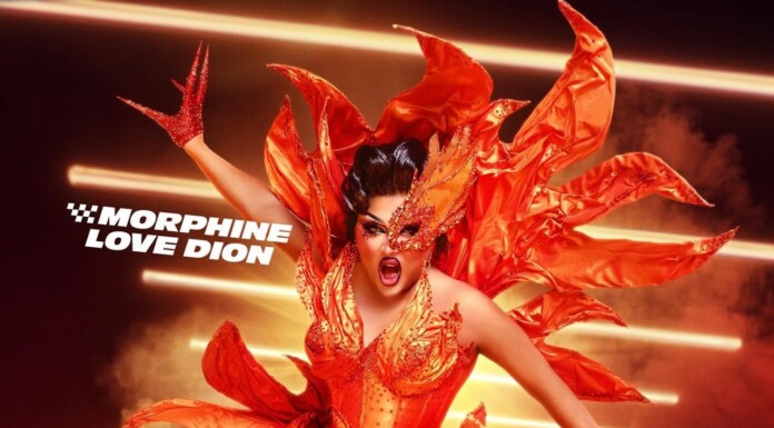 Drag Queen Morphine Love Dion Pushes Back on Fan Pressure to Identify as Trans Drag performer in a fiery orange costume with dramatic makeup, posing against streaks of light.