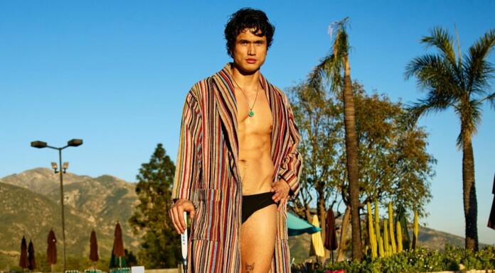 Charles Melton Heats Up Men’s Health Ahead Of Beef Season 2 Premiere Man in a striped robe over black swim briefs posing poolside at a sunny resort with palm trees in the background