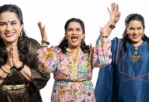 Three smiling women of Indian descent raise their hands in celebration against a white background, wearing colorful outfits and jewelry.