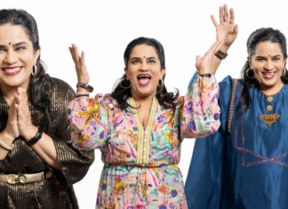 Three smiling women of Indian descent raise their hands in celebration against a white background, wearing colorful outfits and jewelry.
