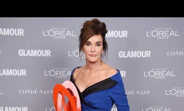 Woman in a blue and black off-shoulder gown on a gray Glamour backdrop, holding an orange circular award; logos for Glamour and L'Oréal Paris visible in the background.
