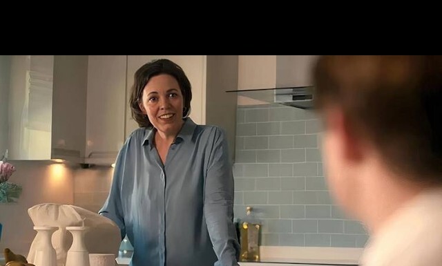 Heartstopper Finale Film Recasts Nick’s Mom Woman in a blue blouse leans on a kitchen counter, smiling at a person whose back is visible in a modern tiled kitchen.