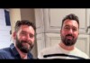 Two men with beards smiling at the camera in a kitchen with light gray cabinets.