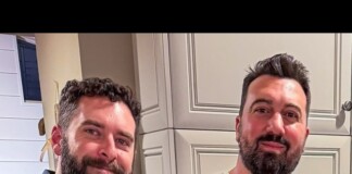 Two men with beards smiling at the camera in a kitchen with light gray cabinets.