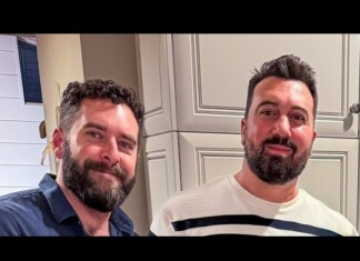 Two men with beards smiling at the camera in a kitchen with light gray cabinets.