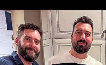 Two men with beards smiling at the camera in a kitchen with light gray cabinets.