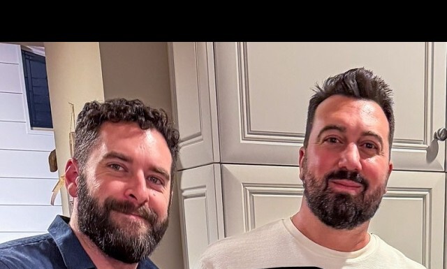 Two men with beards smiling at the camera in a kitchen with light gray cabinets.