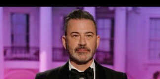 Portrait of a man in a black tuxedo and bow tie, posing in front of a purple-lit backdrop at an event.