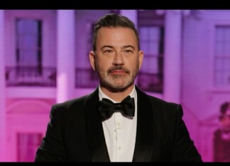 Portrait of a man in a black tuxedo and bow tie, posing in front of a purple-lit backdrop at an event.