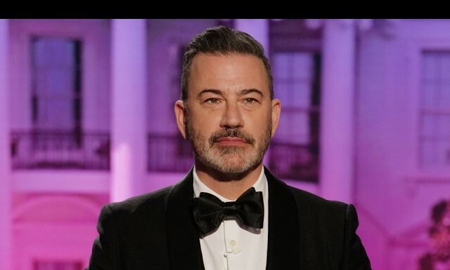Portrait of a man in a black tuxedo and bow tie, posing in front of a purple-lit backdrop at an event.