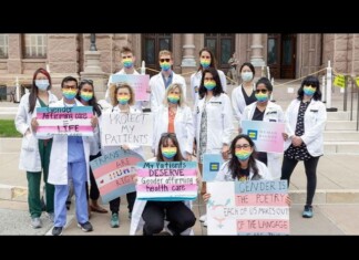 Hospitals Are Still Silent on Resuming Trans Youth Care Even After Court Blocks Federal Threats Group of students in white coats with rainbow masks holding signs advocating gender-affirming care and LGBTQ rights on courthouse steps.