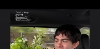 Young man in a car, smiling with pink and green flowers in the foreground; text overlay reads 'That's a wrap BABY' with social handles (joelocke03, sam__max).