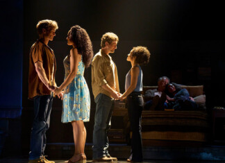 The Notebook’s Broadway Touring Company – Comes to the Kravis and Arsht Centers Four actors stand in two couples on a dimly lit stage, holding hands as if in rehearsal, with a couple seated on a sofa in the background.