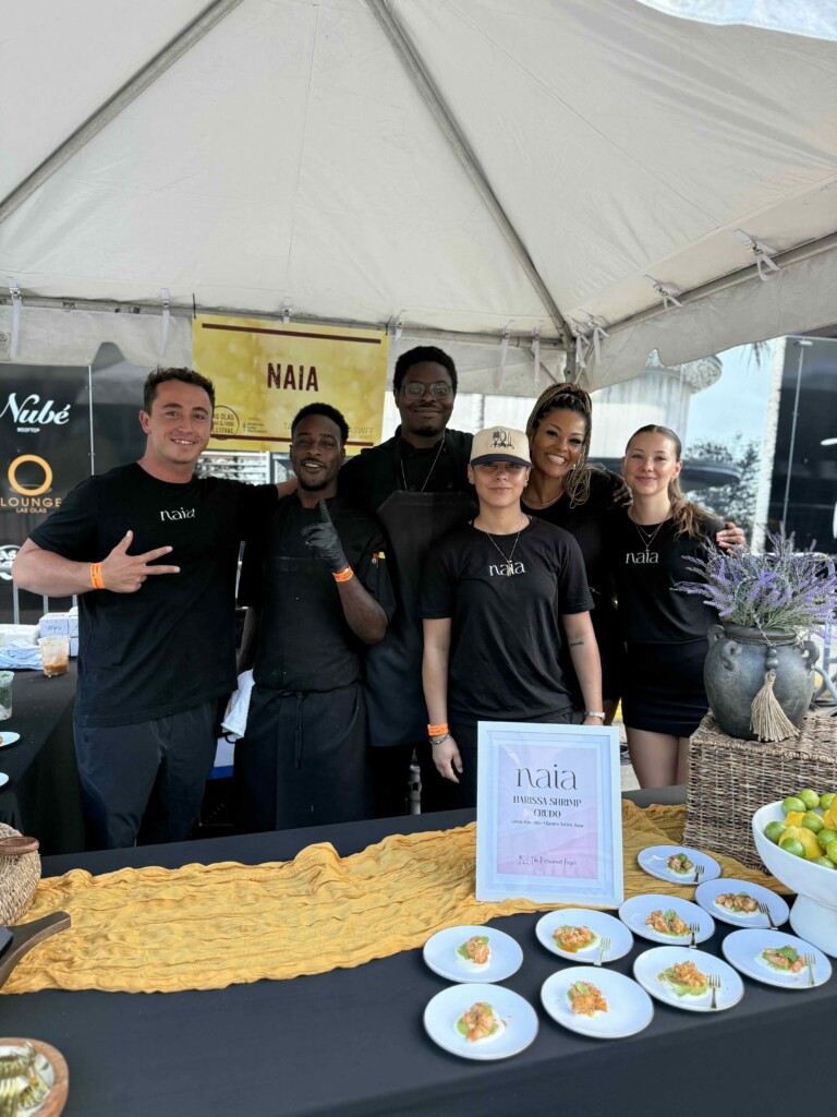 Six people in black shirts under a tent, posing and smiling for a group photo at a food stall.