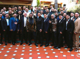 Large group of men in suits and a few women in formalwear pose on an orange-tiled terrace at a formal event.