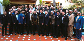 Large group of men in suits and a few women in formalwear pose on an orange-tiled terrace at a formal event.