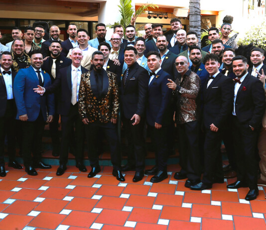 Large group of men in suits and a few women in formalwear pose on an orange-tiled terrace at a formal event.