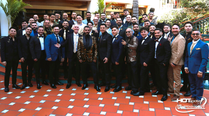 Large group of men in suits and a few women in formalwear pose on an orange-tiled terrace at a formal event.