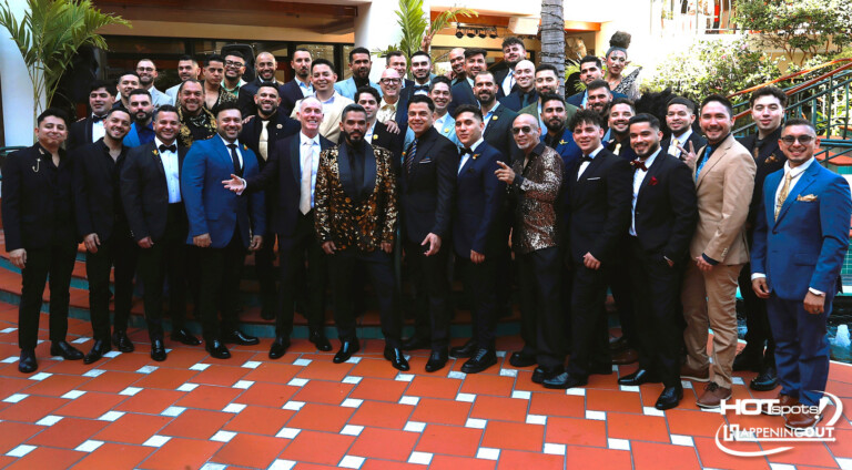 Large group of men in suits and a few women in formalwear pose on an orange-tiled terrace at a formal event.