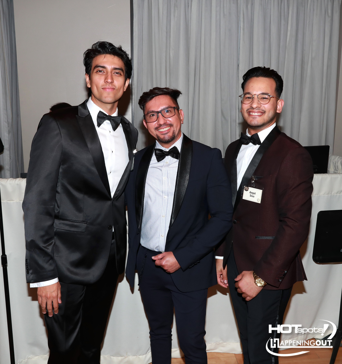 Three men in tuxedos posing and smiling for a photo at a formal event.