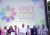 Group of eight people posing on a stage in front of a colorful Out Shine LGBTQ+ Film Festival banner reading Miami & Fort Lauderdale.