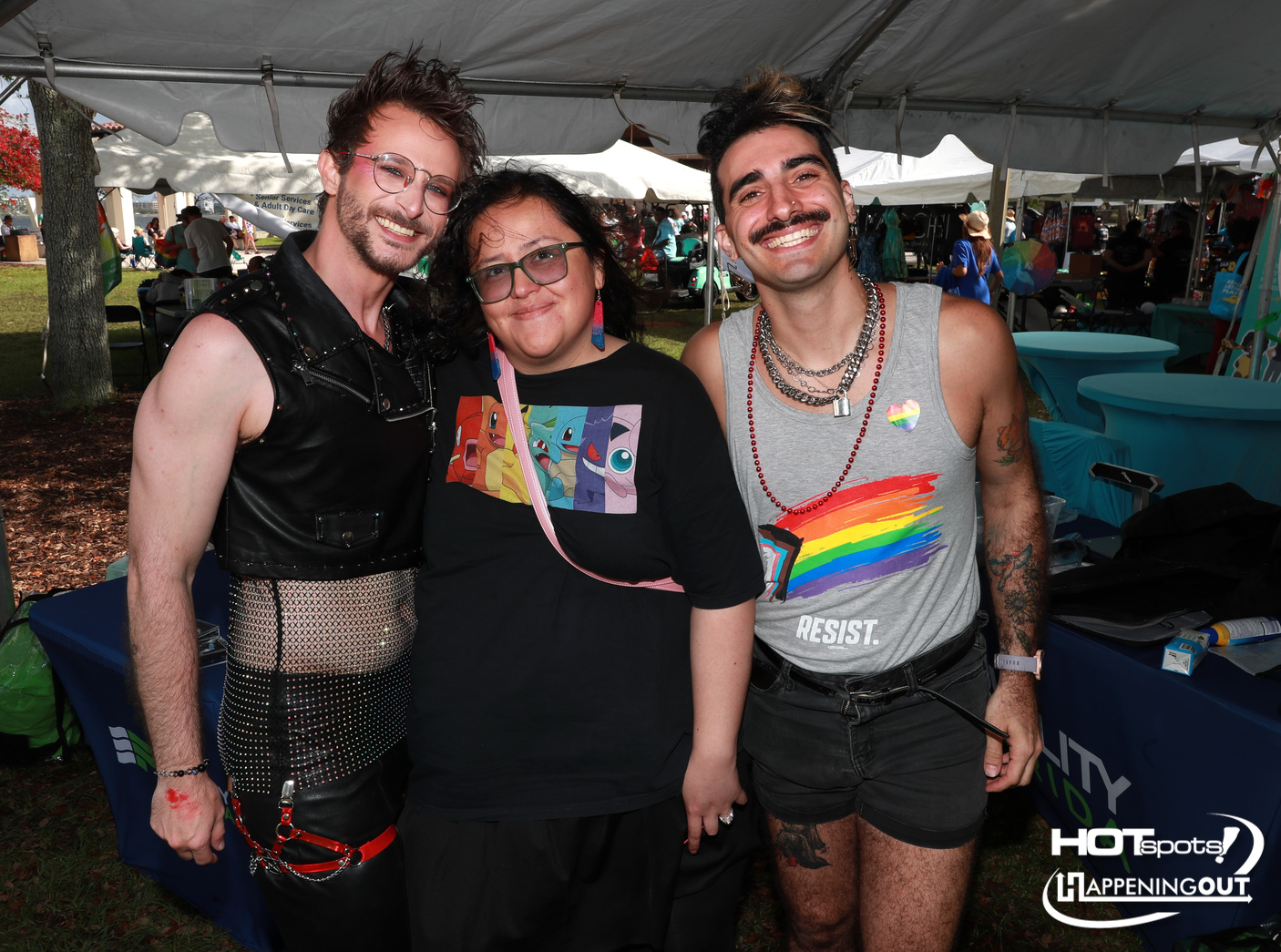 Three friends pose and smile at an outdoor festival under a large white tent.