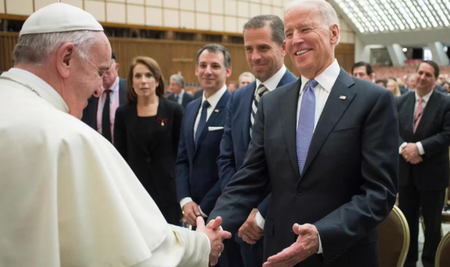 DOJ Report Labels Biden LGBTQ+ Policies Anti-Christian, Proposes Rollbacks Religious leader in white robes shakes hands with a man in a dark suit at a formal event, with several attendees in business attire in the background.