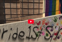 Video thumbnail showing graffiti on a concrete wall: the text 'pride is' with multicolored handprints around it and a red play button overlay in the center.