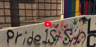 Video thumbnail showing graffiti on a concrete wall: the text 'pride is' with multicolored handprints around it and a red play button overlay in the center.