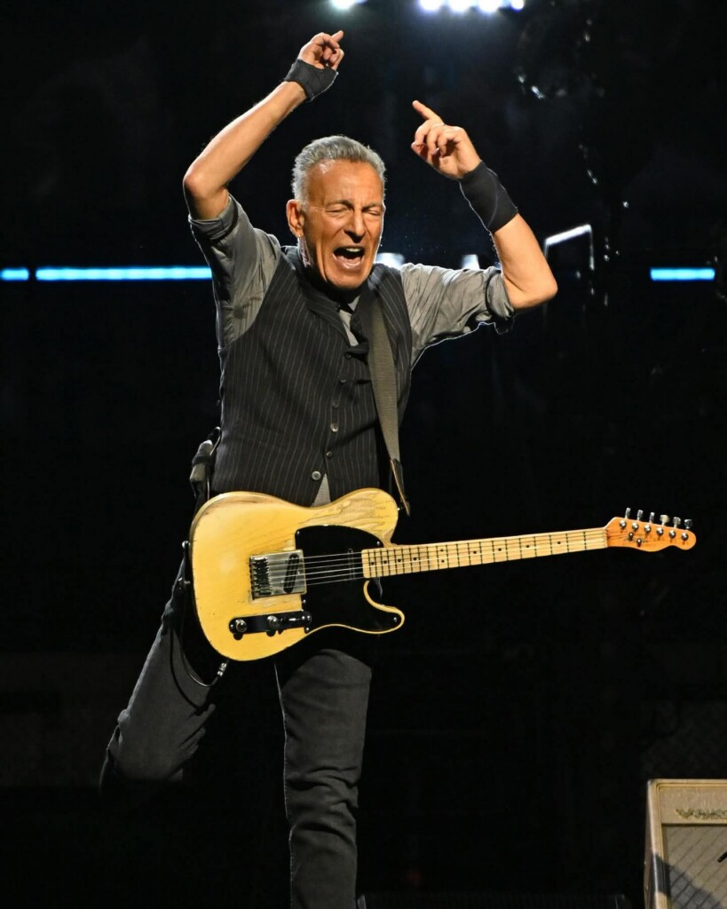 Male guitarist on stage raising arms in celebration while playing a light-colored Fender Telecaster.