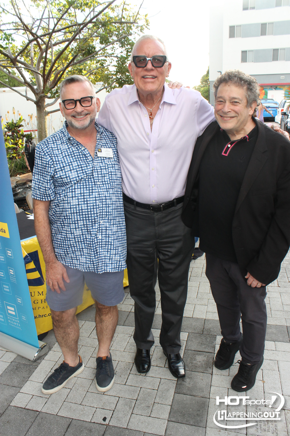 Three men pose together outdoors at an event, smiling at the camera.